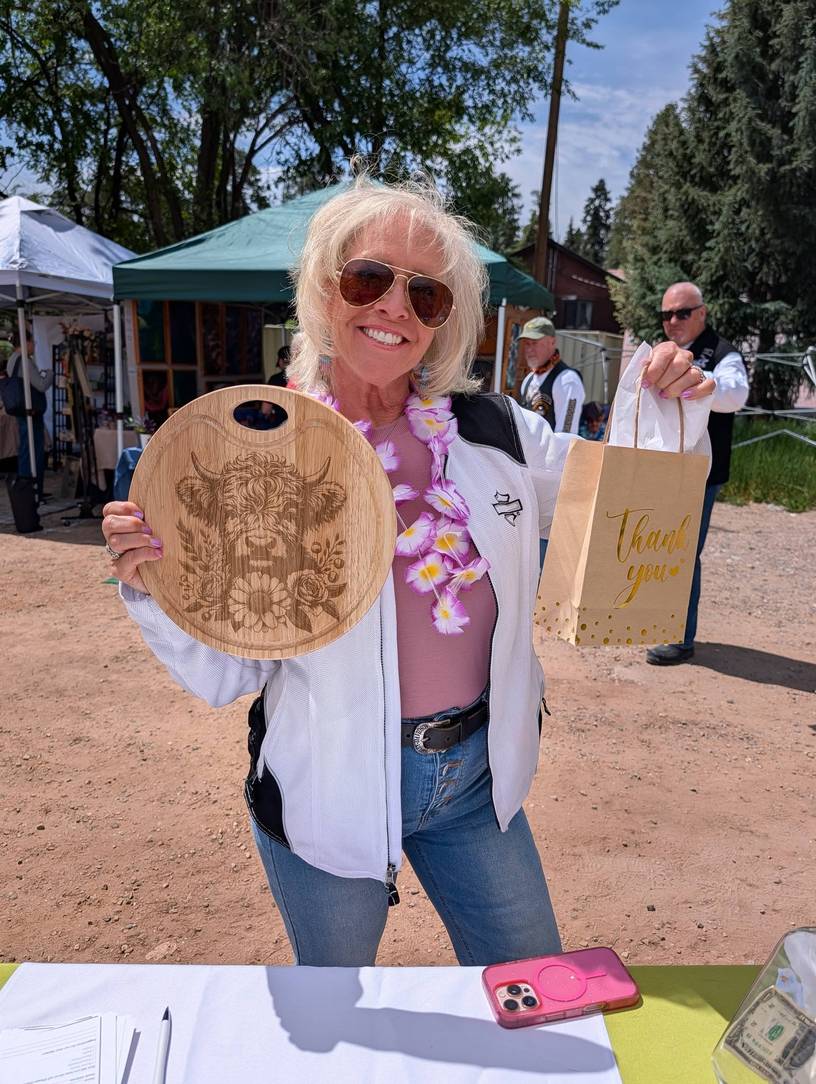 A happy shopper holding a laser-engraved wood board at the Pondering Pines Maker's Market