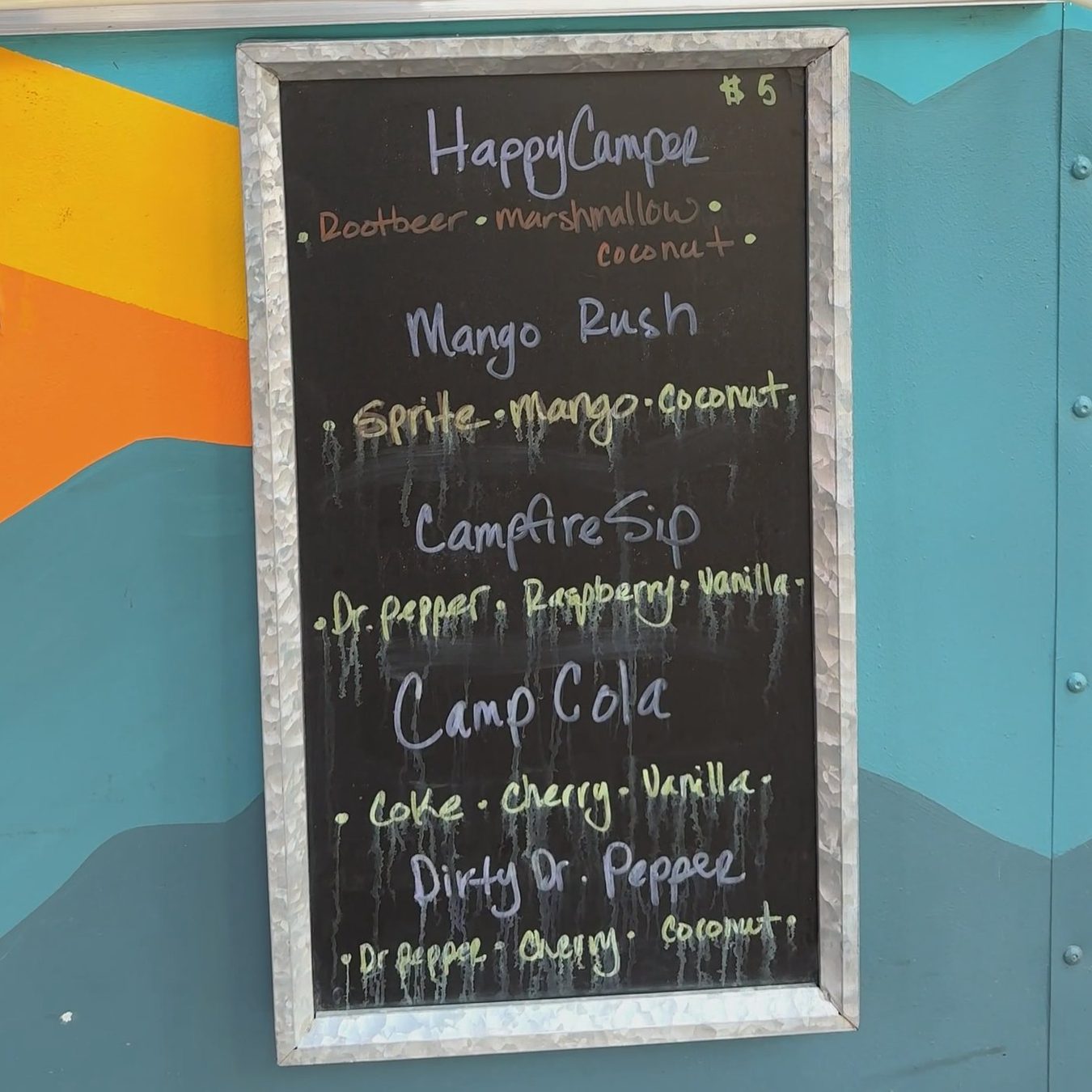 The camp soda chalkboard on the trailer: Happy Camper, Mango Rush, Campfire Sip, Camp Cola and Dirty Dr. Pepper