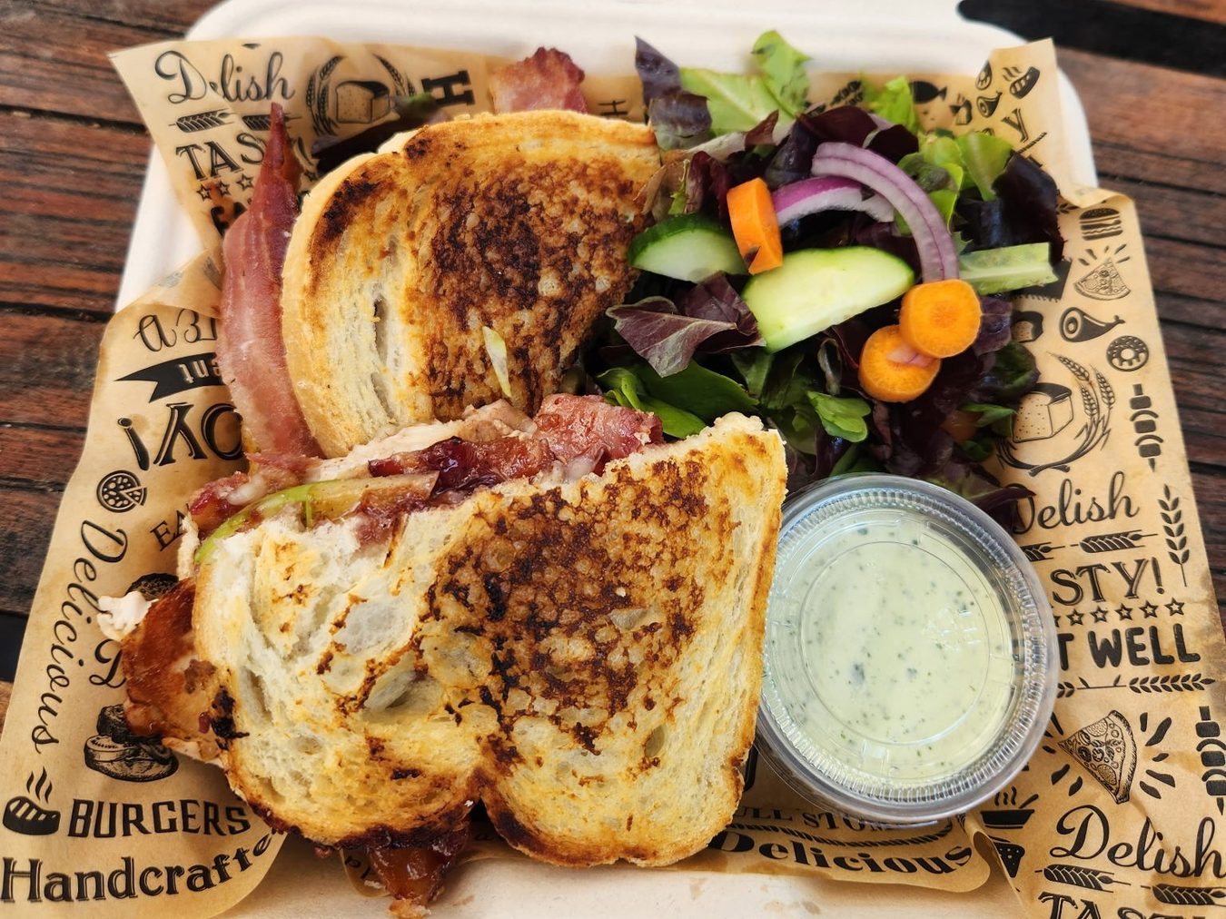 Two grilled sourdough melts with bacon beside a side salad and a cup of green sauce